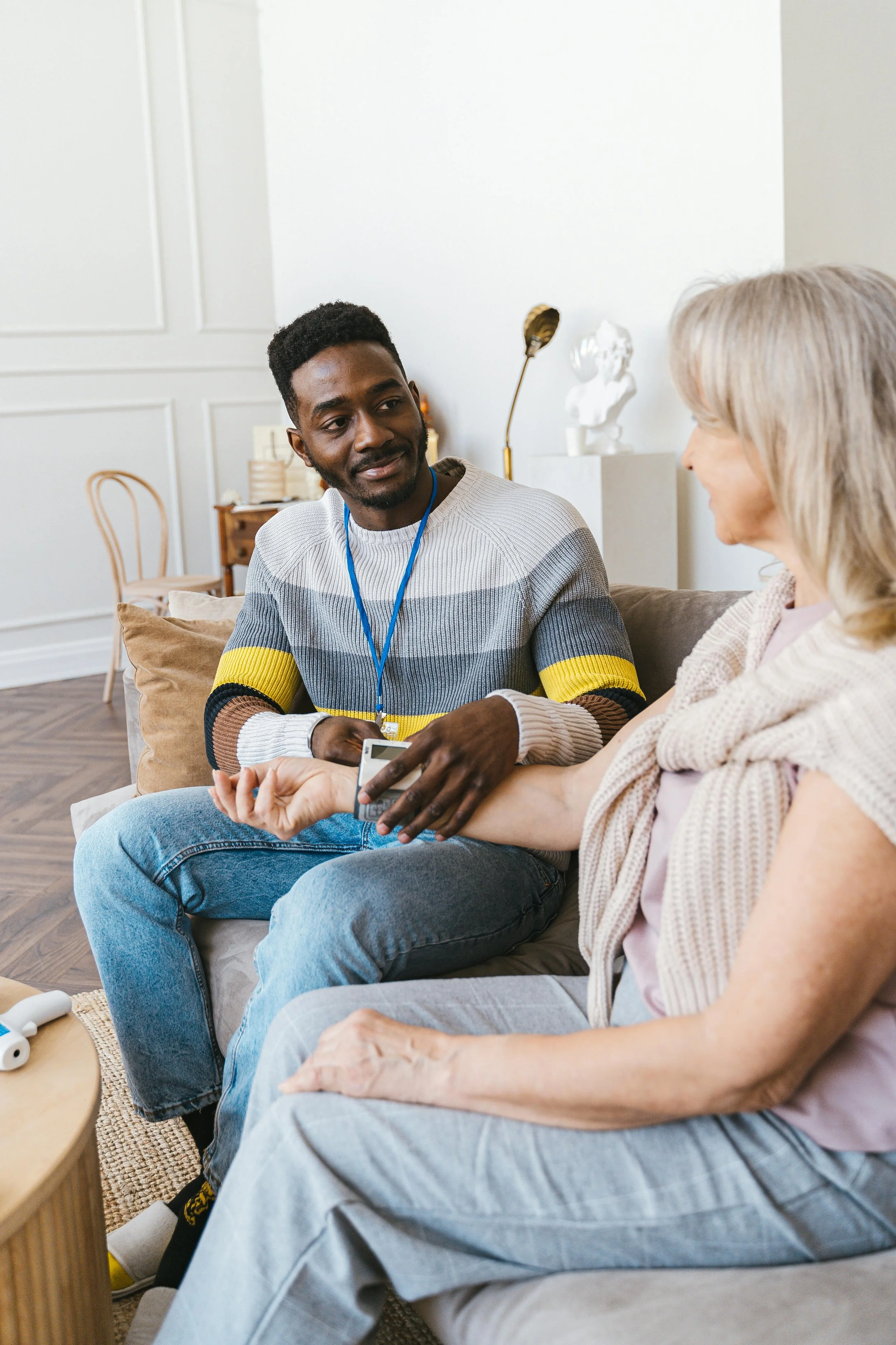 A young black man and an older white woman sitting together on a sofa having a conversation. The man is smiling and holding a smartphone, while the woman is reaching out to touch his handBrightmane Therapeutic Center decorative illustration