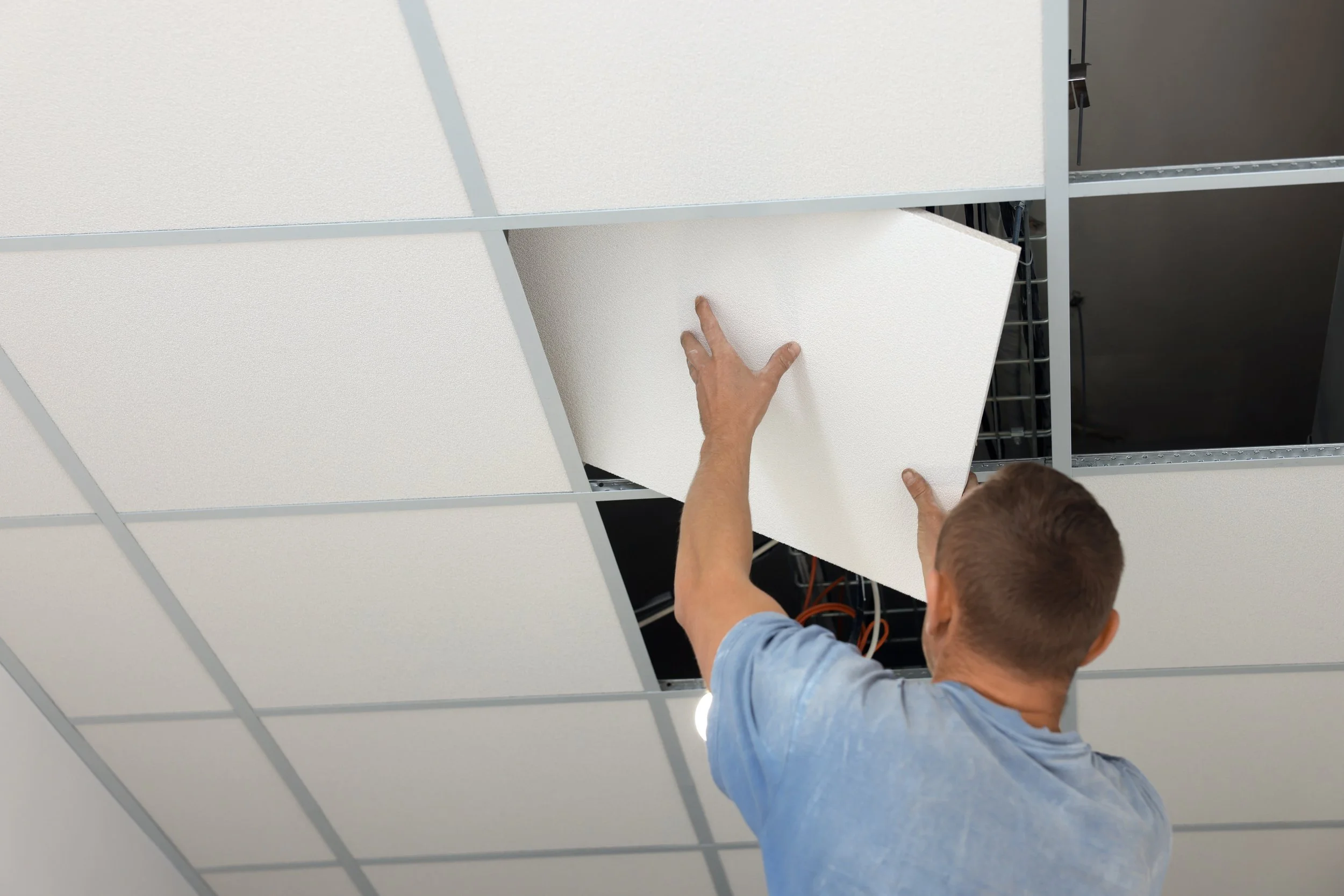 Technician installing a ceiling tile in an office drop ceiling grid.