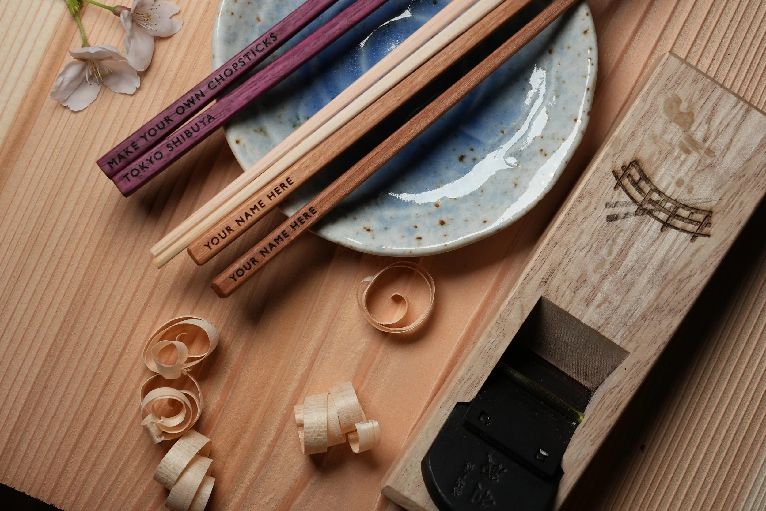 Various chopsticks that have custom engravings, a cermaic dish, wood shavings, and wooden box on a wooden surface. Make Your Own Chopsticks, Shibuya, Shinjuku, Tokyo, Japan, Japanese, Asakusa. Handmade.