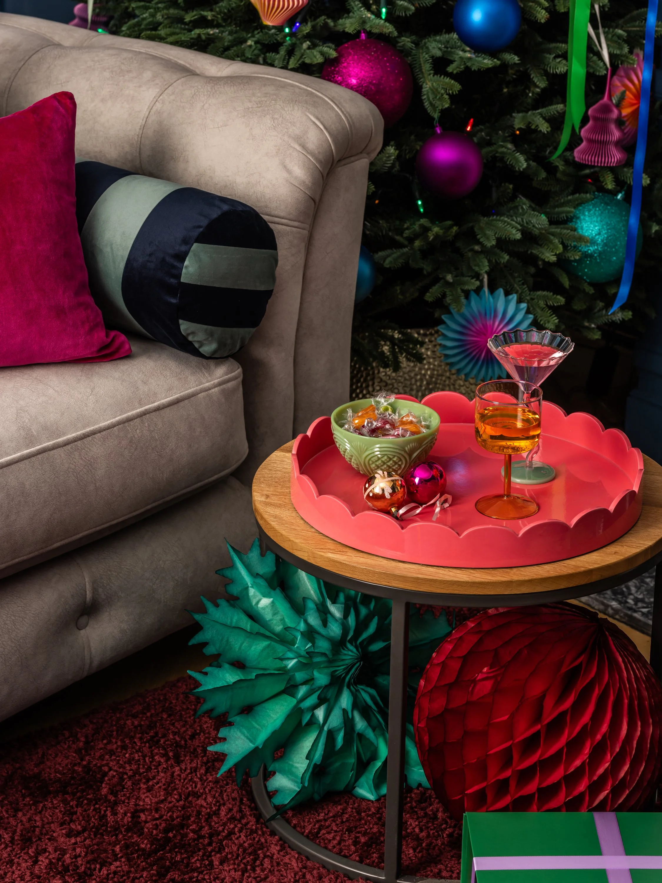 A cozy holiday scene with a decorated Christmas tree, a beige sofa with colorful pillows, and a small round table with festive decorations and drinks.