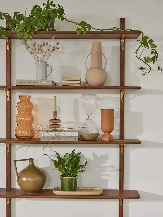 Decorative wooden wall shelf with plants, vases, and books, arranged with a mix of modern and rustic decor on a white wall.