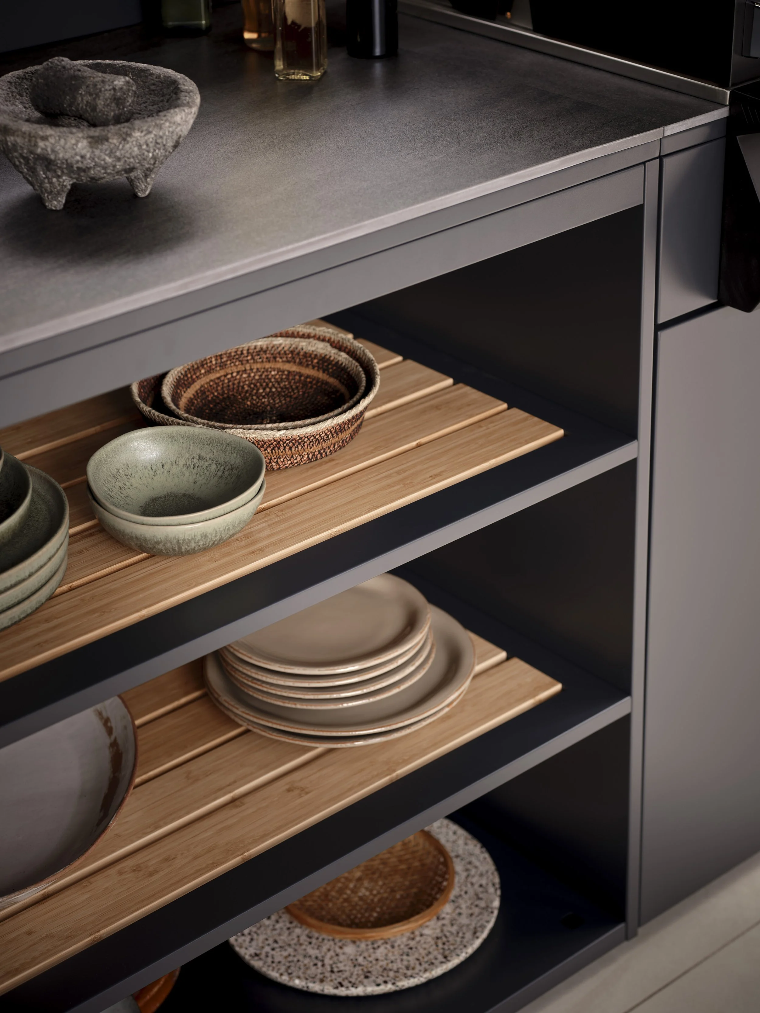Kitchen cabinet with open shelves containing ceramic bowls and plates, along with a decorative stone mortar and pestle on the countertop.