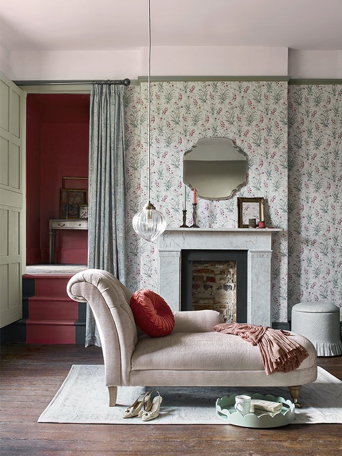 Living room with a chaise lounge, red pillows, fireplace, mirror, floral wallpaper, and a staircase in the background.