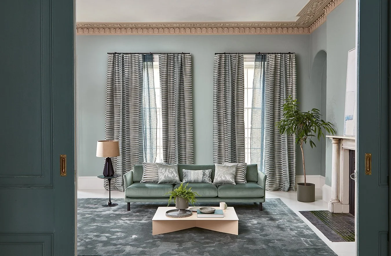 Living room with blue walls, striped curtains, green sofa, black side table with lamp, marble fireplace, potted plant, and modern decor.