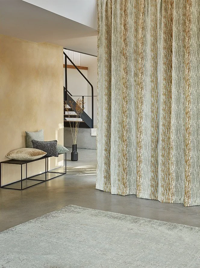 Modern interior with archway, textured curtains, bench with pillows, and a staircase in the background.
