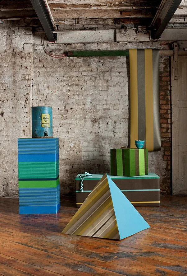 Colorful geometric sculpture displayed in an industrial space with exposed brick wall and wooden floor.