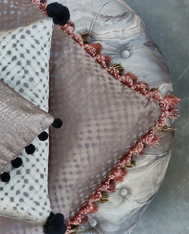 Close-up of decorative pillows on a tufted marble or stone surface, featuring textured fabrics and pom-pom trim.