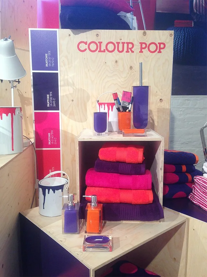 Display of colorful towels, lotion bottles, and paint-themed decor with a color palette chart on a wooden board.