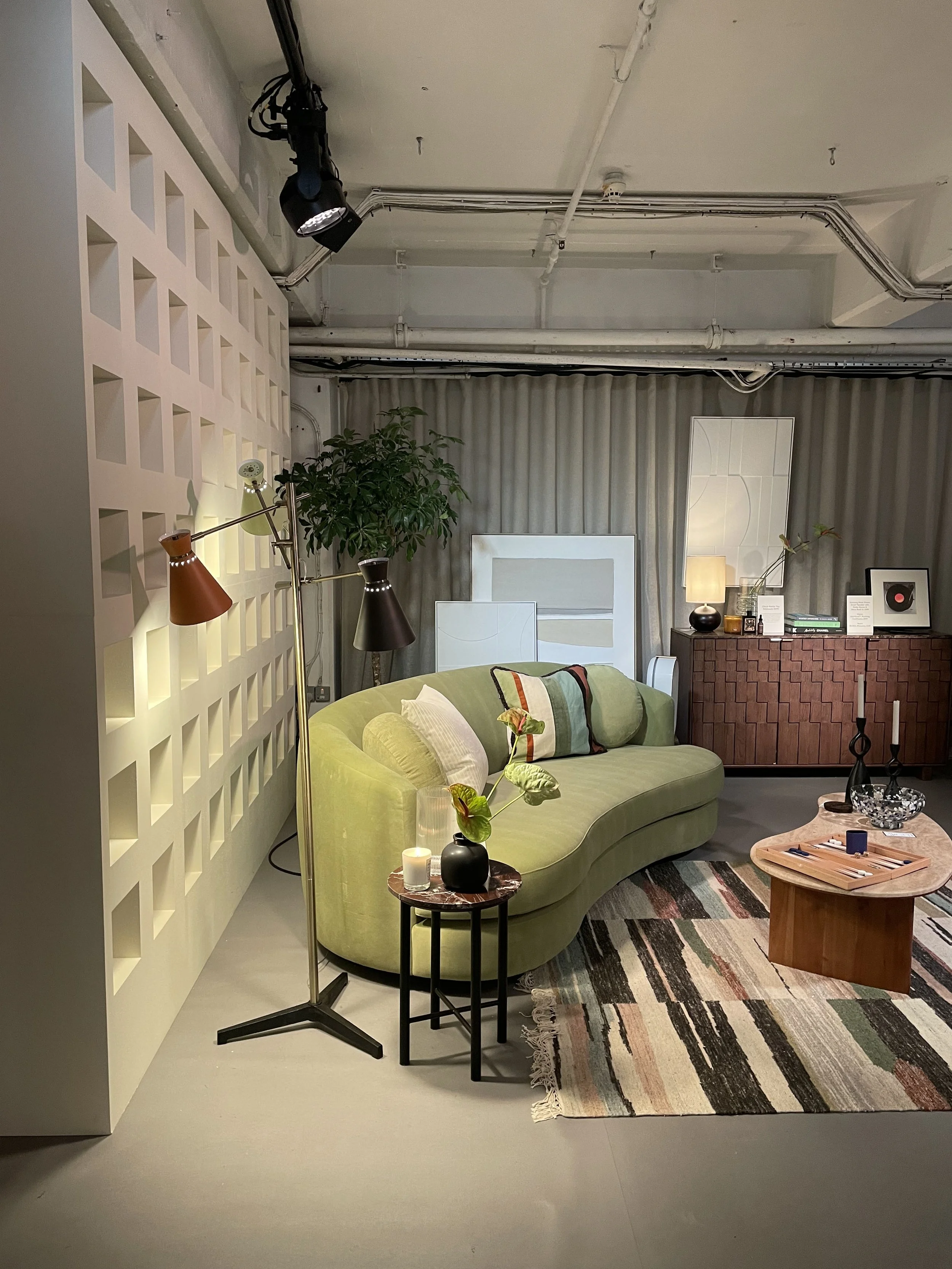 Living room with a green sofa, black side table with a black vase, striped rug, abstract wall art, and a wooden coffee table with decor items.