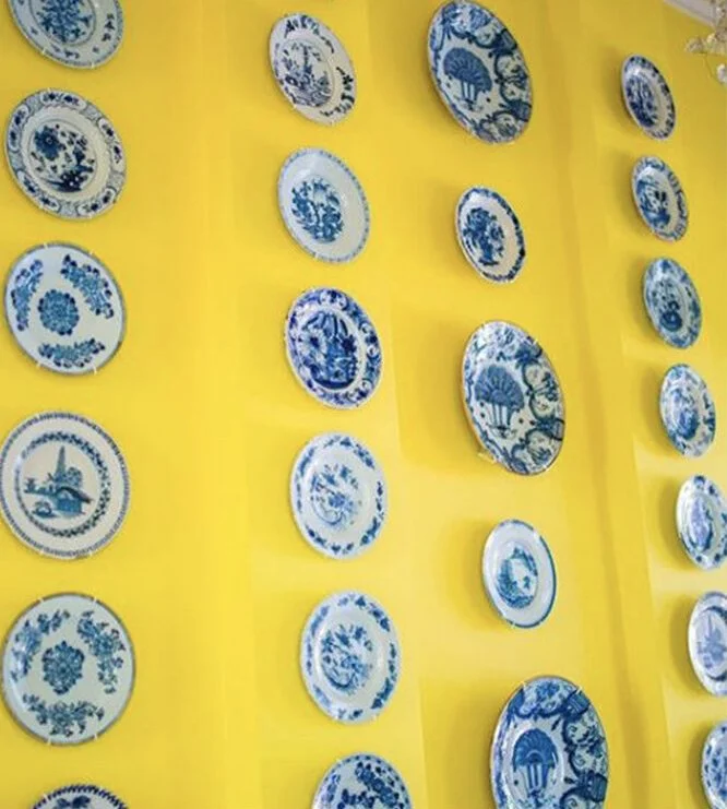 Collection of blue and white decorative plates displayed on a yellow wall.