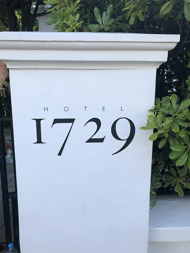 White hotel sign with the word "HOTEL" and the number "1729" displayed in black text, surrounded by green bushes.