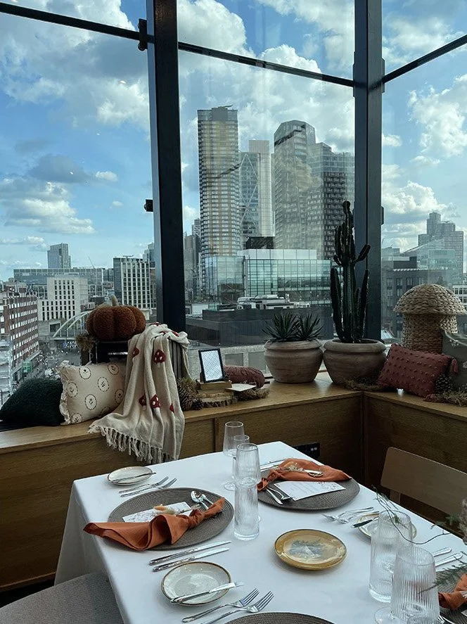 Chinese city skyline viewed from a restaurant with large glass windows, decorated with potted plants, pillows, and tableware for dining.