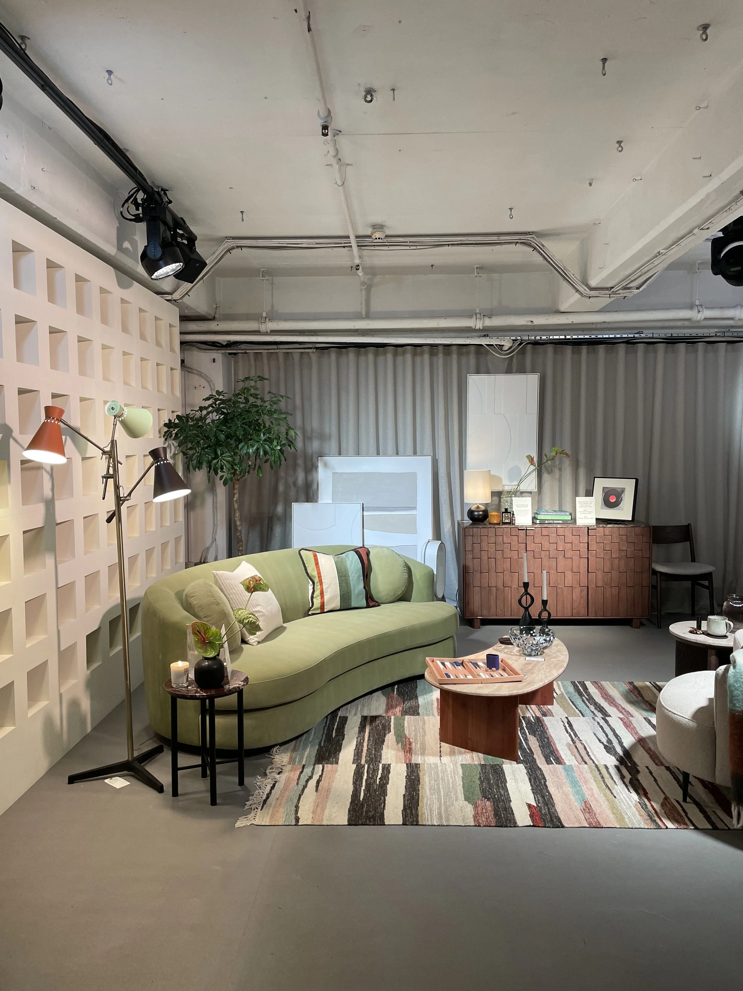 Living room with green sofa, multicolored striped rug, side tables, art prints, wooden cabinet, and decorative items in a cozy, modern style.