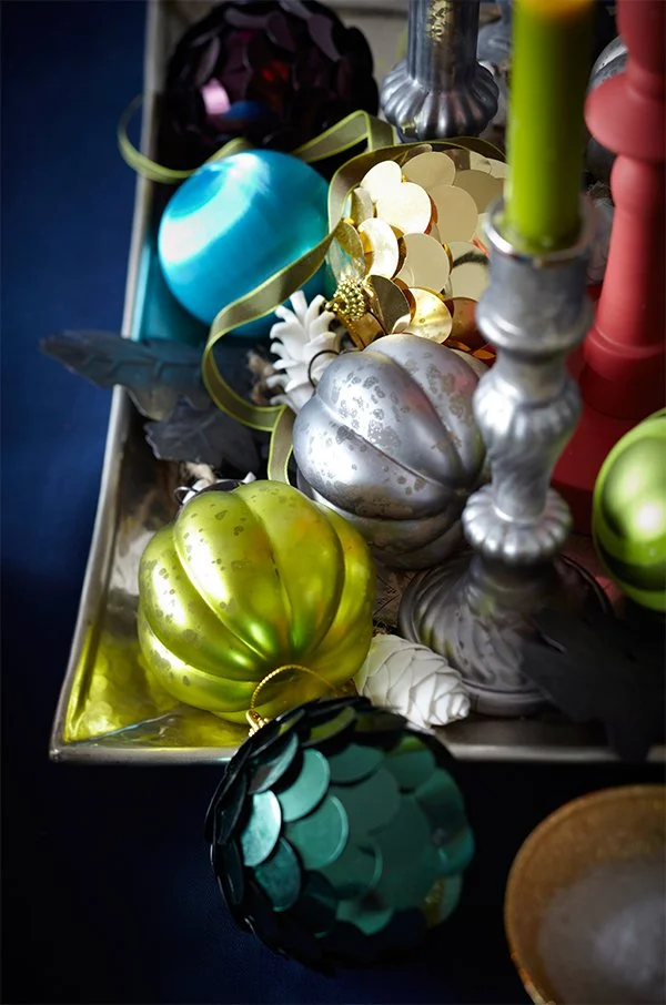 Decorative Christmas ornaments including shiny silver, green, blue, and black baubles, some with textured surfaces, along with ornate candle holders and other holiday decorations in a tray.
