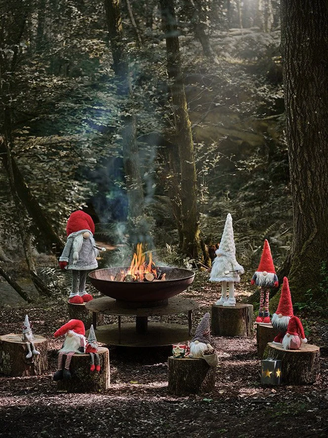 Decorative gnomes in a forest around a campfire with trees in the background.