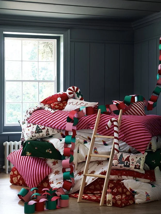 Christmas-themed bed with colorful stockings, elf slippers, and garland in a cozy, decorated room with a window.