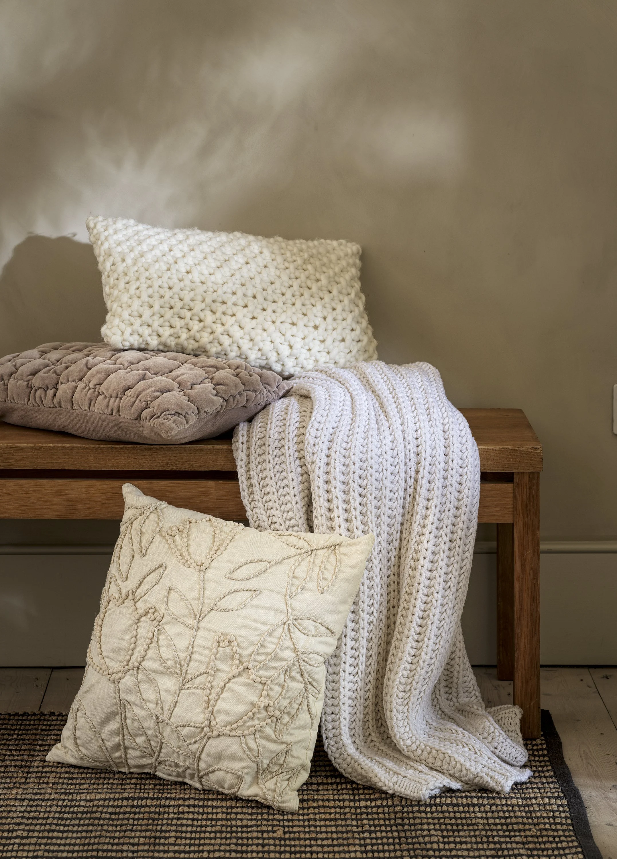 Decorative pillows and a chunky knit blanket on a wooden bench in a cozy living room.