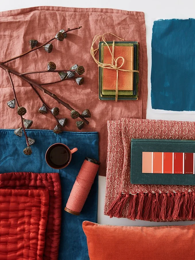Flat lay of fabric swatches, a paint sample card, a cup of coffee, some dried seed pods on a branch, a spool of thread, and a watercolor paint strip on paper.