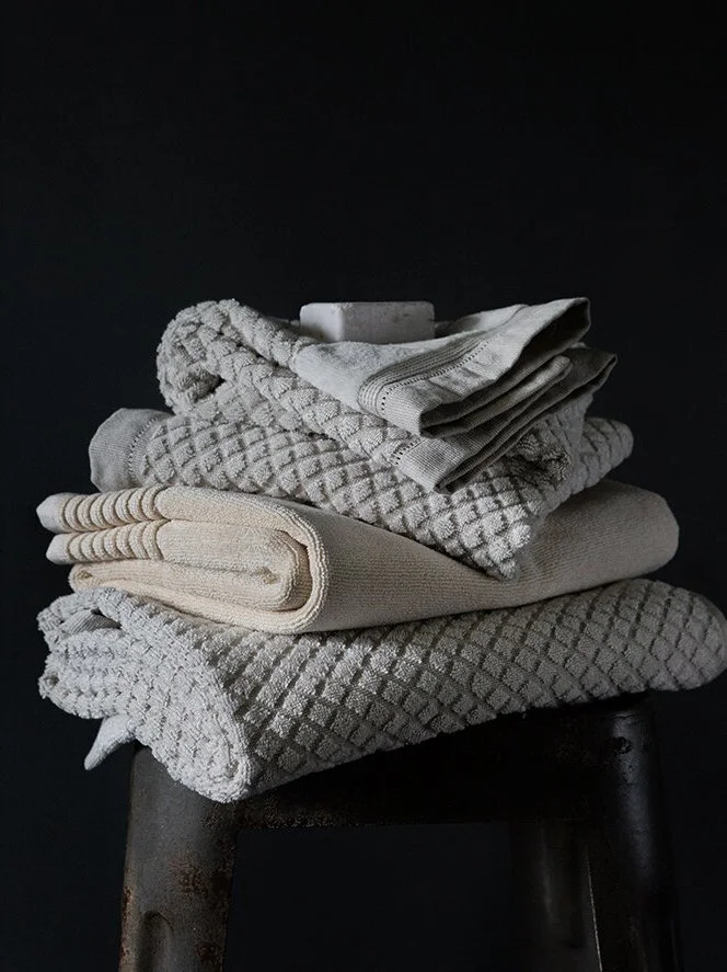 A stack of folded white and gray towels placed on a dark stool against a dark background.