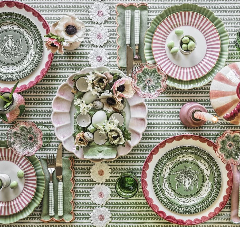 Colorful table setting with patterned plates, teacup, candles, flowers, and decorative ornaments on a striped tablecloth.