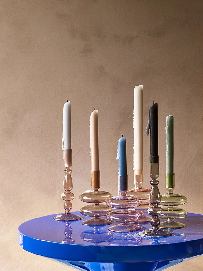 Colorful candles on glass candlesticks arranged on a blue table.