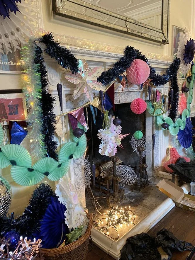 Decorated fireplace with colorful paper ornaments, tinsel, and string lights, creating a festive setting.