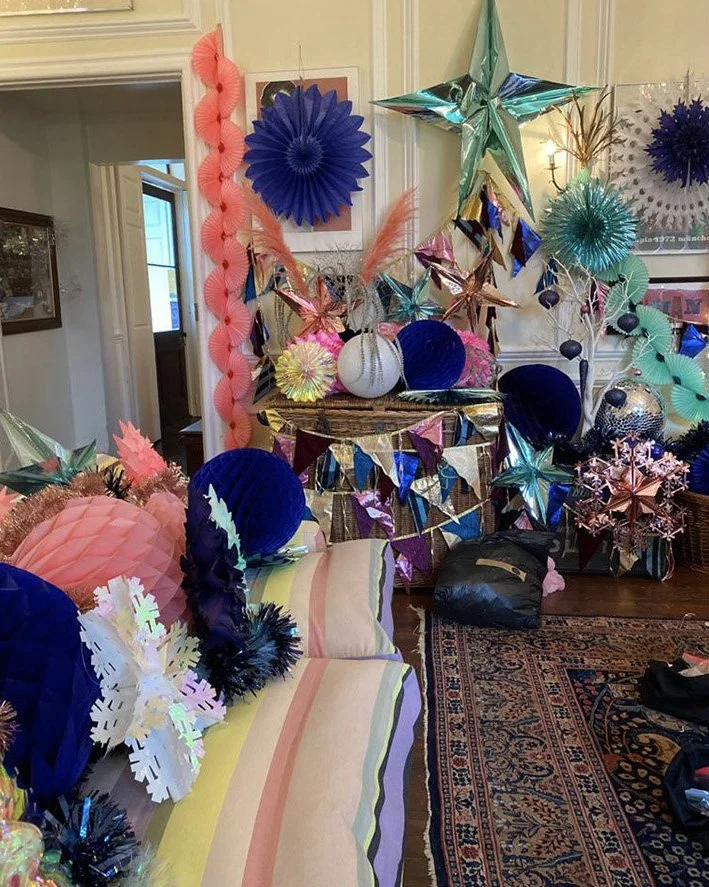 Decorated room with colorful paper and foil stars, paper lanterns, and a striped couch for a festive celebration.