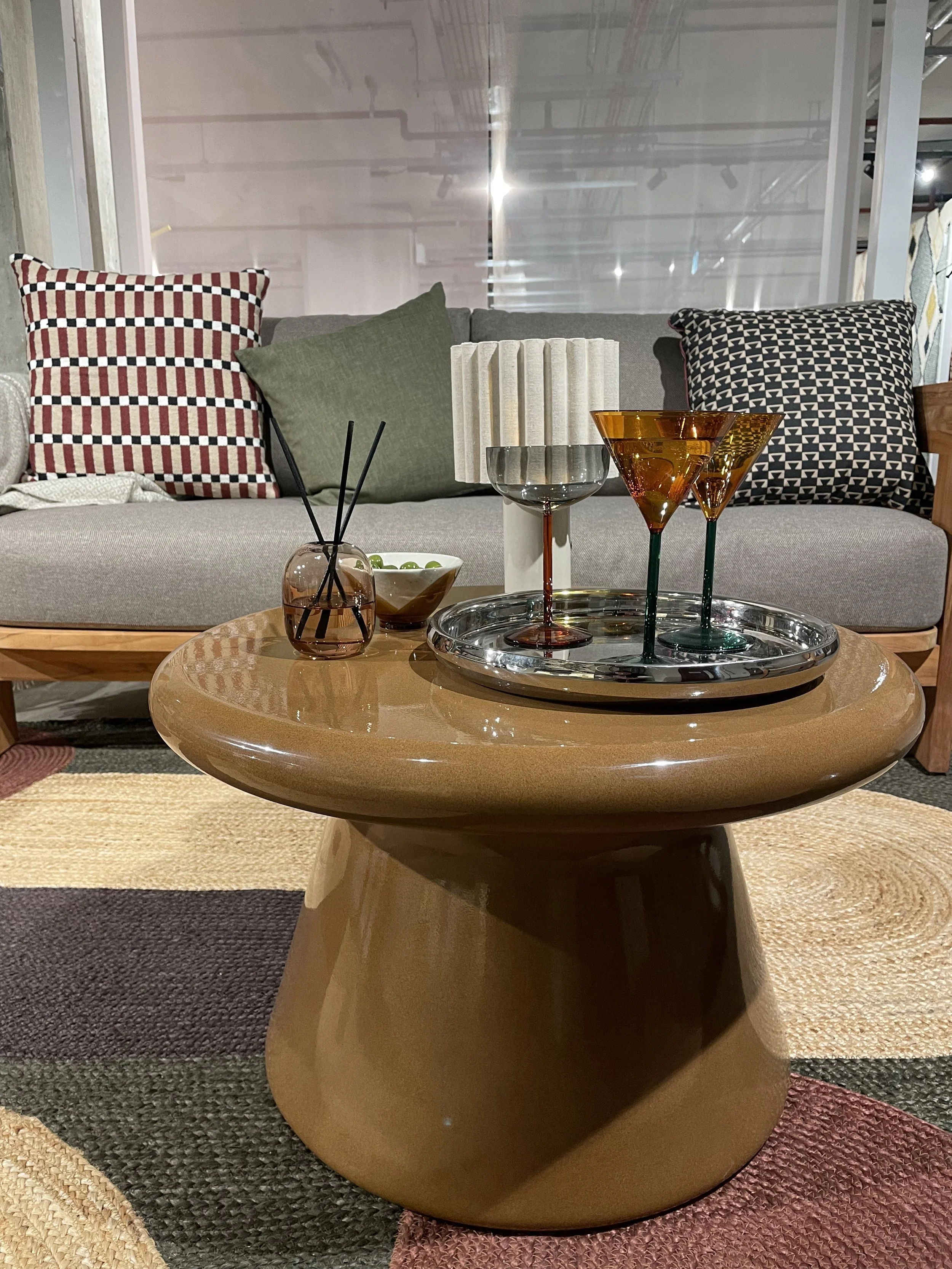 A wooden coffee table with decorative glasses and a diffuser, in front of a sofa with patterned pillows on a rug.