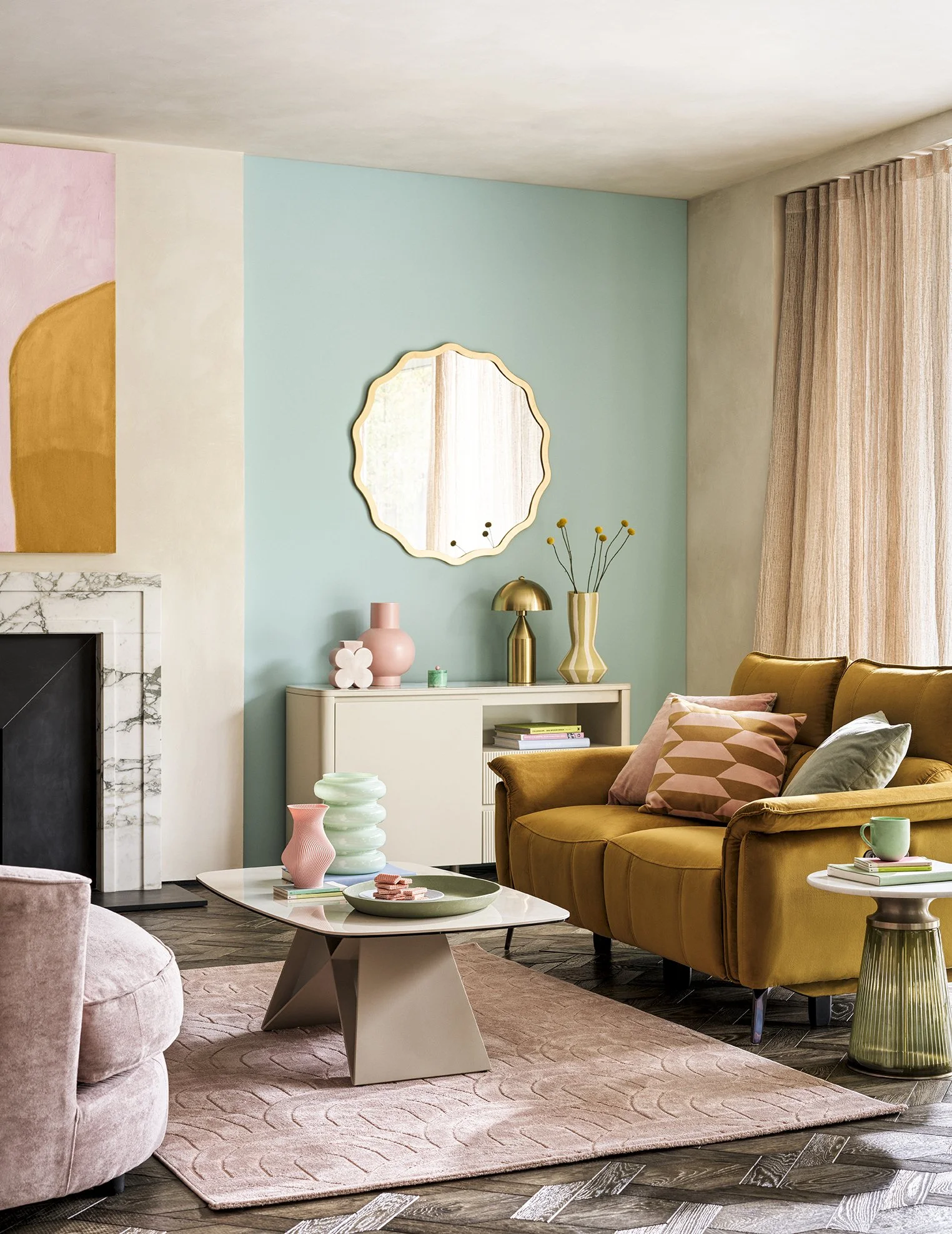 A colorful living room with a pink, mint green, and cream color scheme, featuring a mustard yellow sofa with patterned pillows, a modern coffee table with pink and green vases, a pink rug, and a white cabinet with decorative items, a mirror, and curt