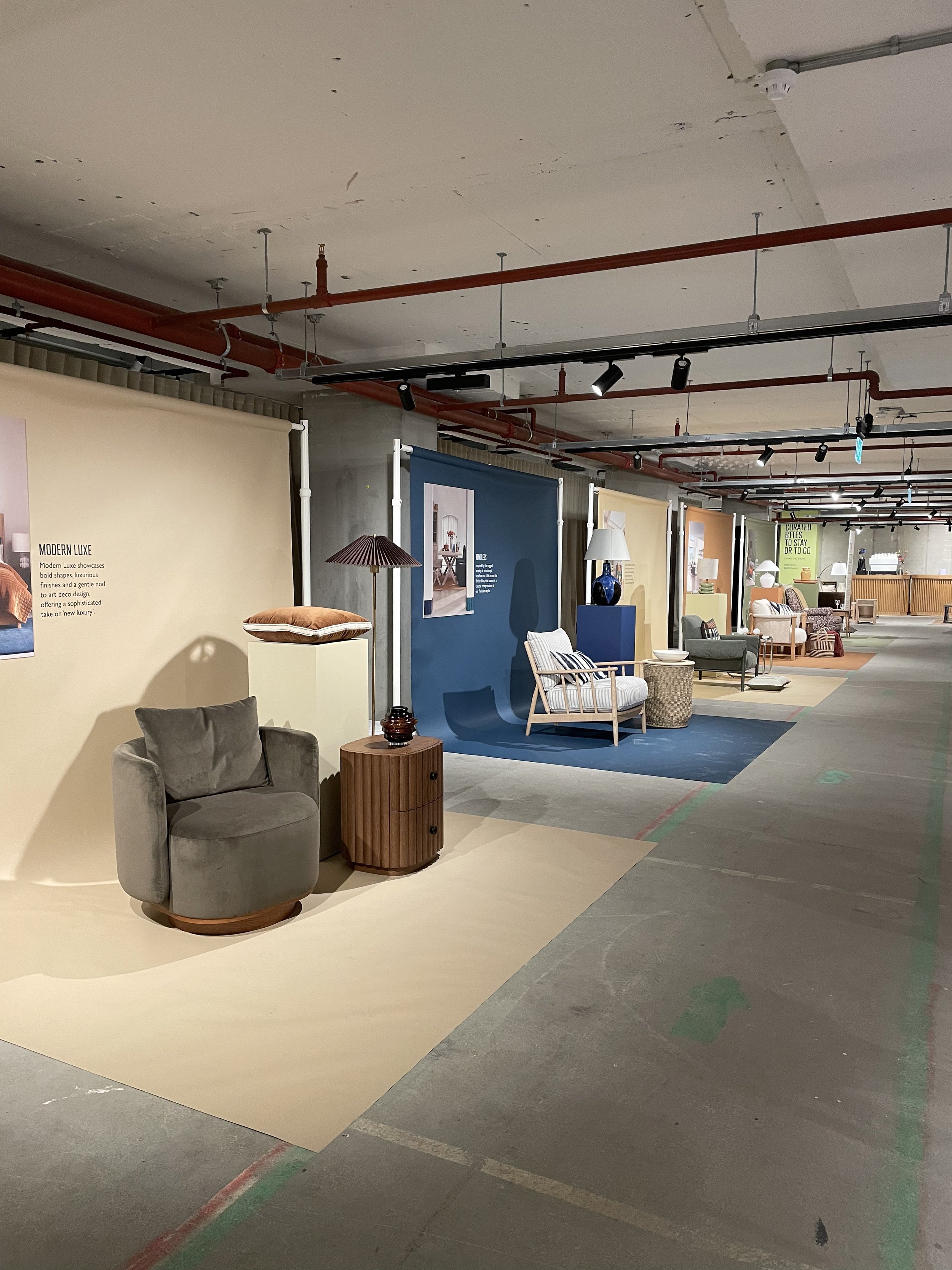 Interior of a furniture showroom displaying various chairs, lamps, and decor items arranged on different colored rugs.