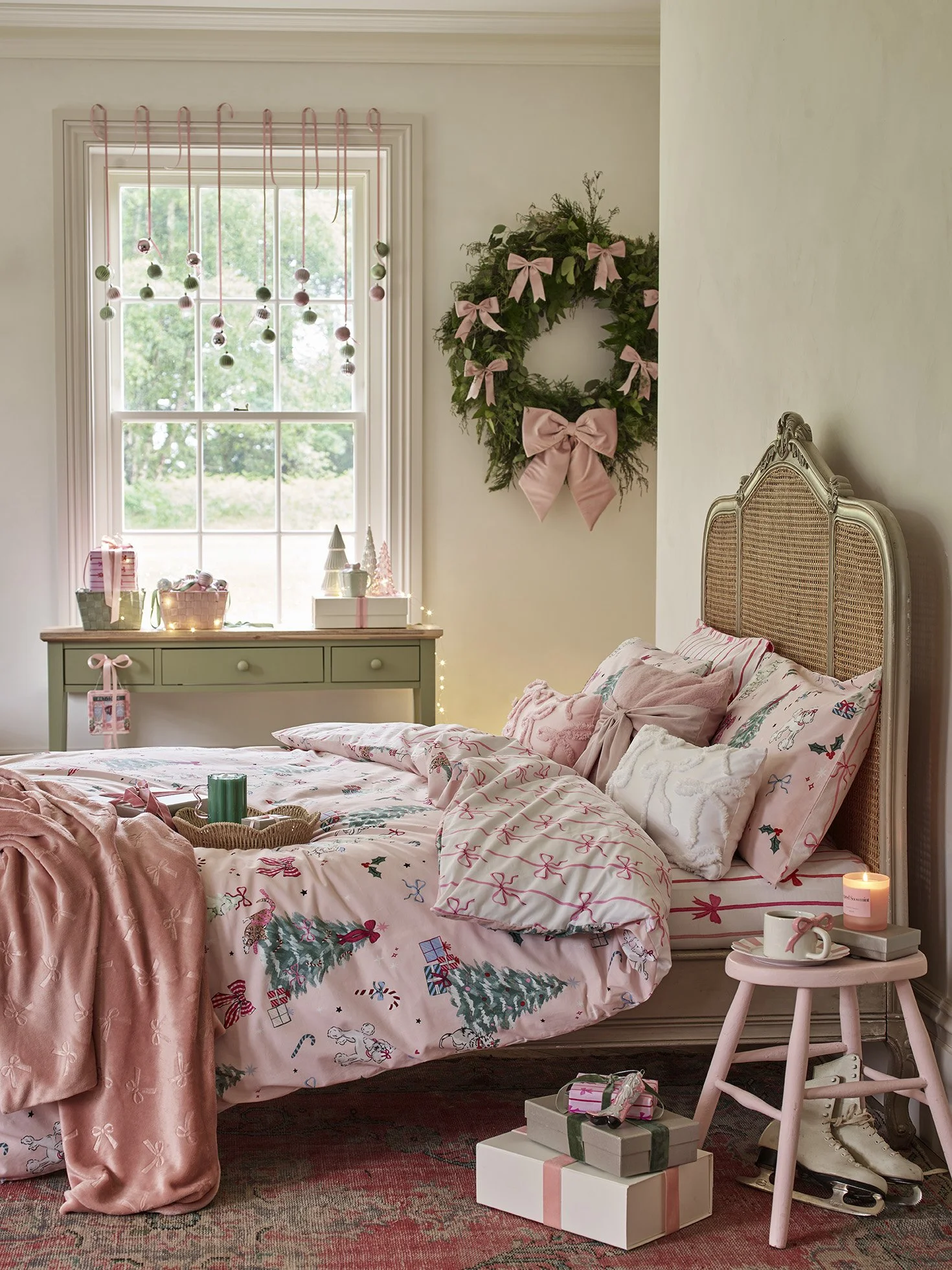 A cozy bedroom decorated for Christmas with pink accents, Christmas cake, wrapped presents, a wreath, and hanging ornaments.