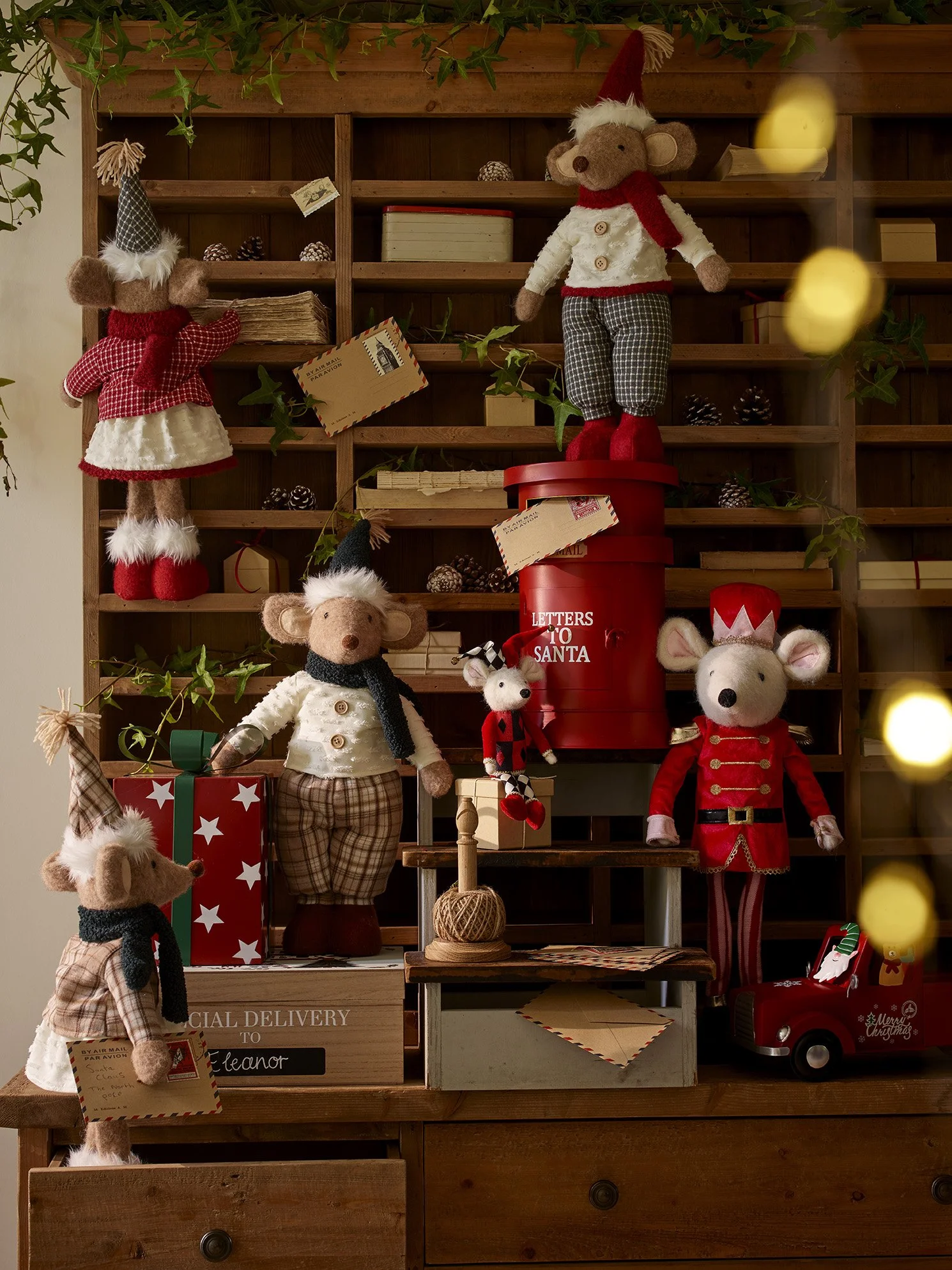 Christmas-themed plush toys and decorations on a wooden shelf, including mice and reindeer dressed in festive clothing, along with holiday boxes and a red mailbox labeled 'Letters to Santa'.
