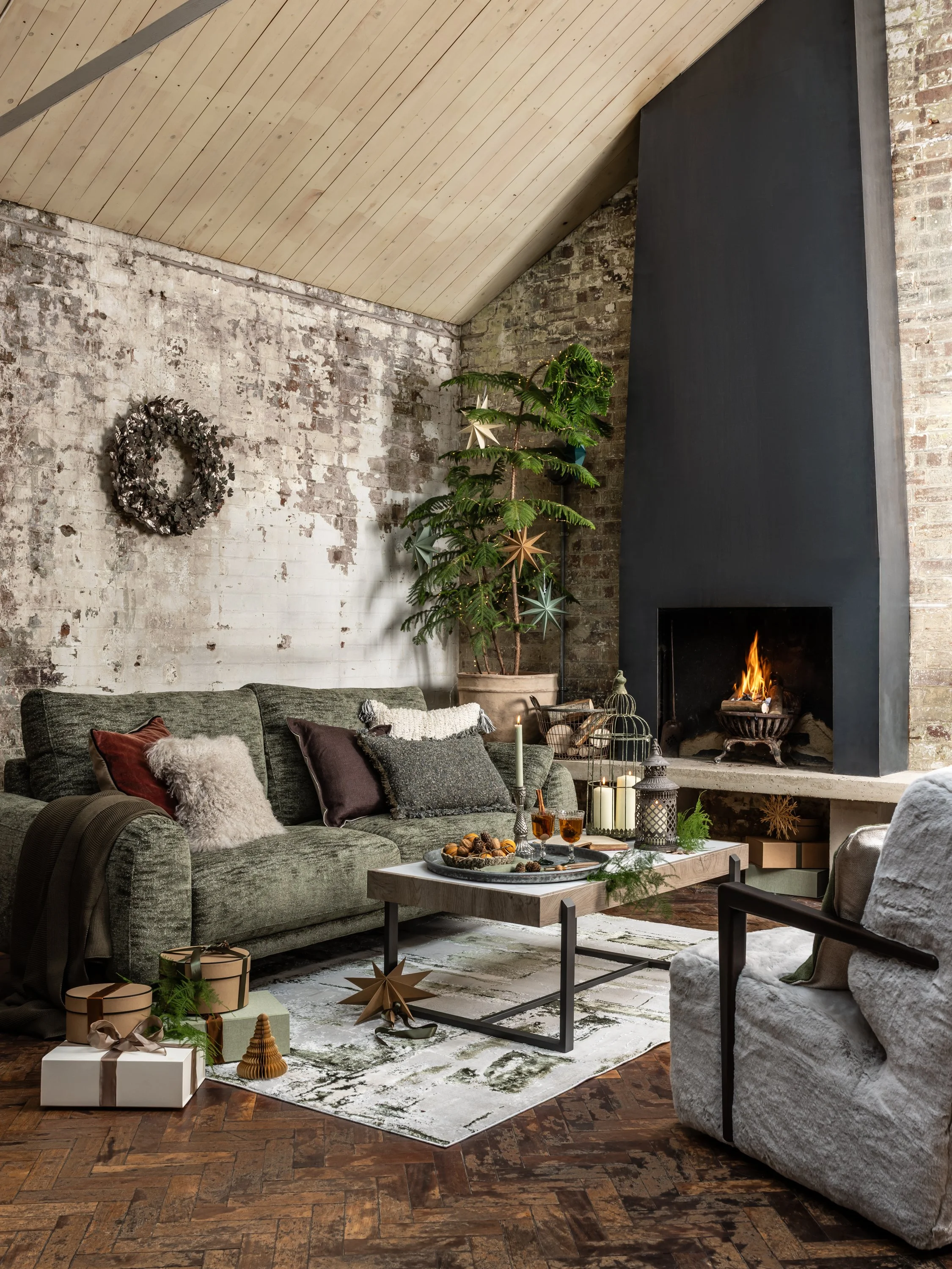 A living room decorated for Christmas with a sofa, armchair, fireplace, and holiday decorations.