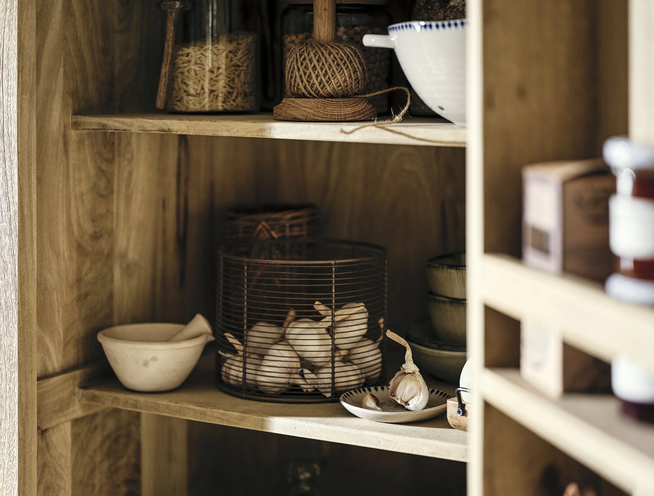 Inside a wooden kitchen cabinet containing garlic bulbs, bowls, and woven baskets.