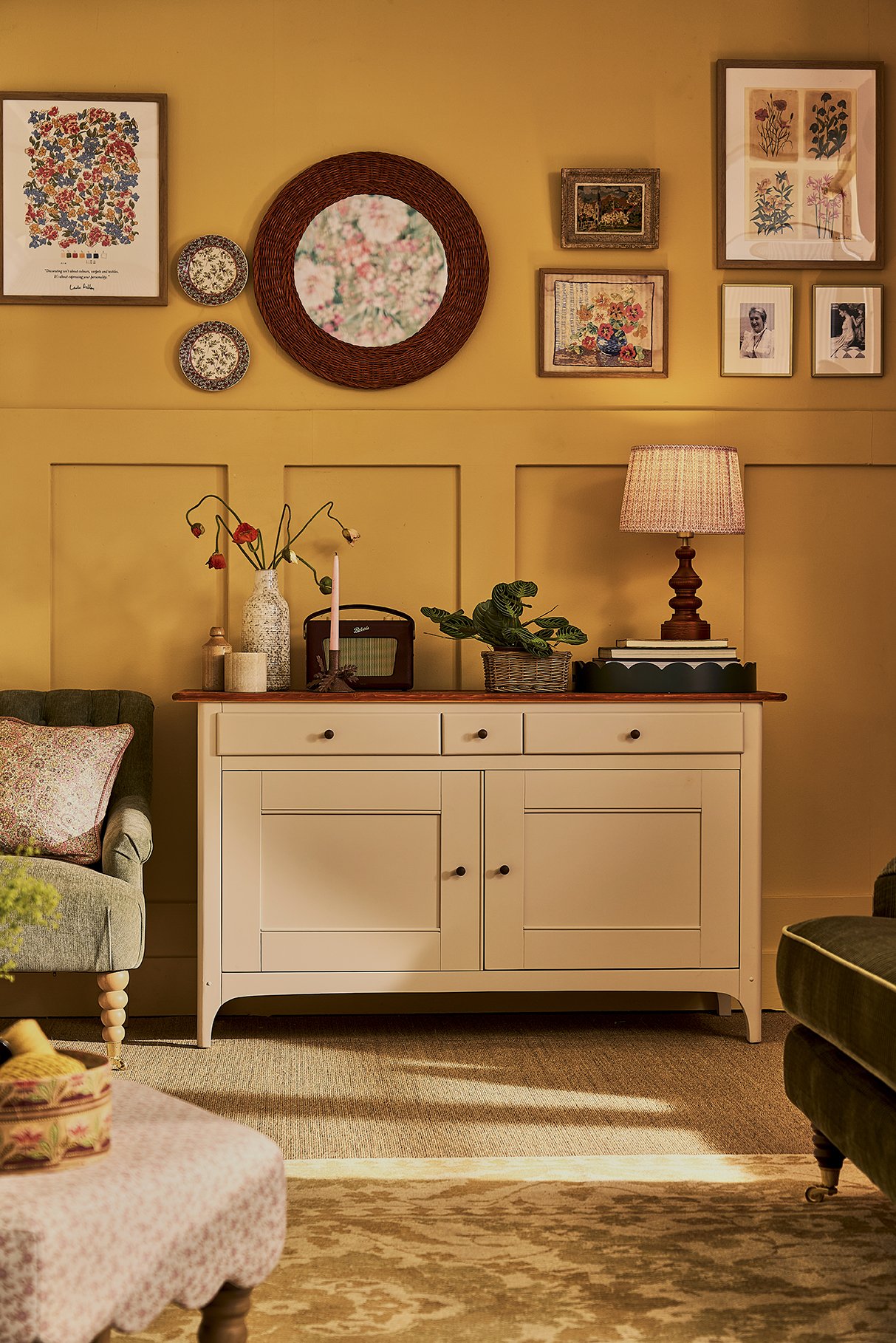 Living room scene with a white sideboard, a table lamp, plants, and framed artwork on a yellow wall.