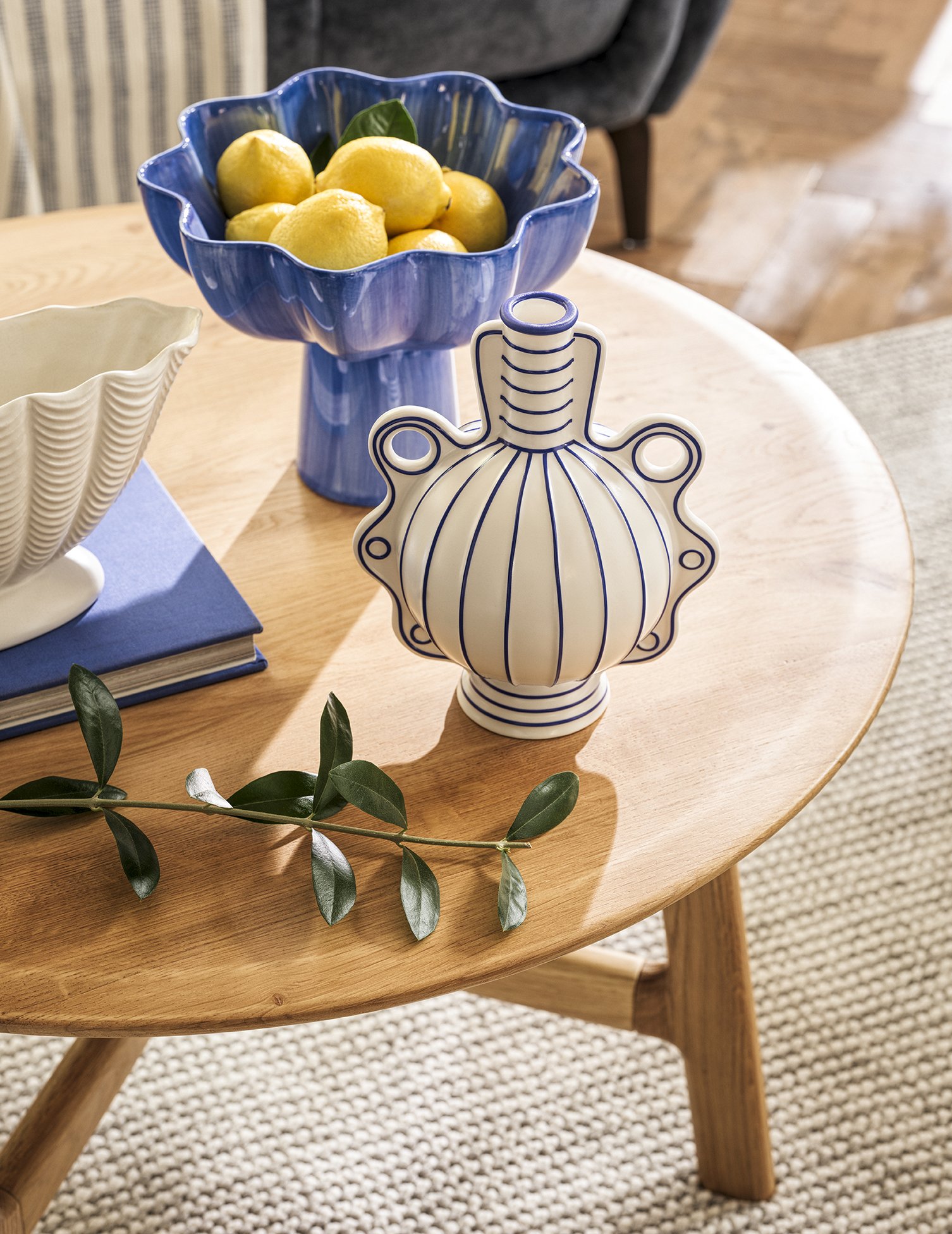 Decorative blue and white vases, a bowl of lemons, and a green branch on a wooden table.