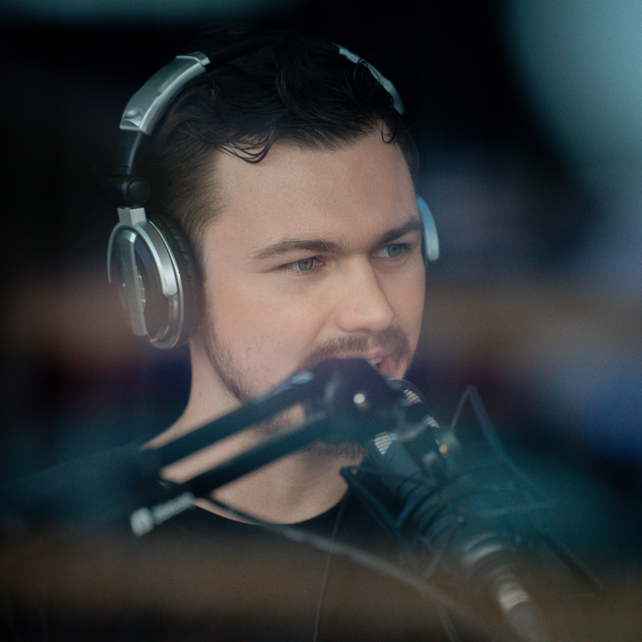 A man with dark hair, wearing headphones, speaking into a microphone.