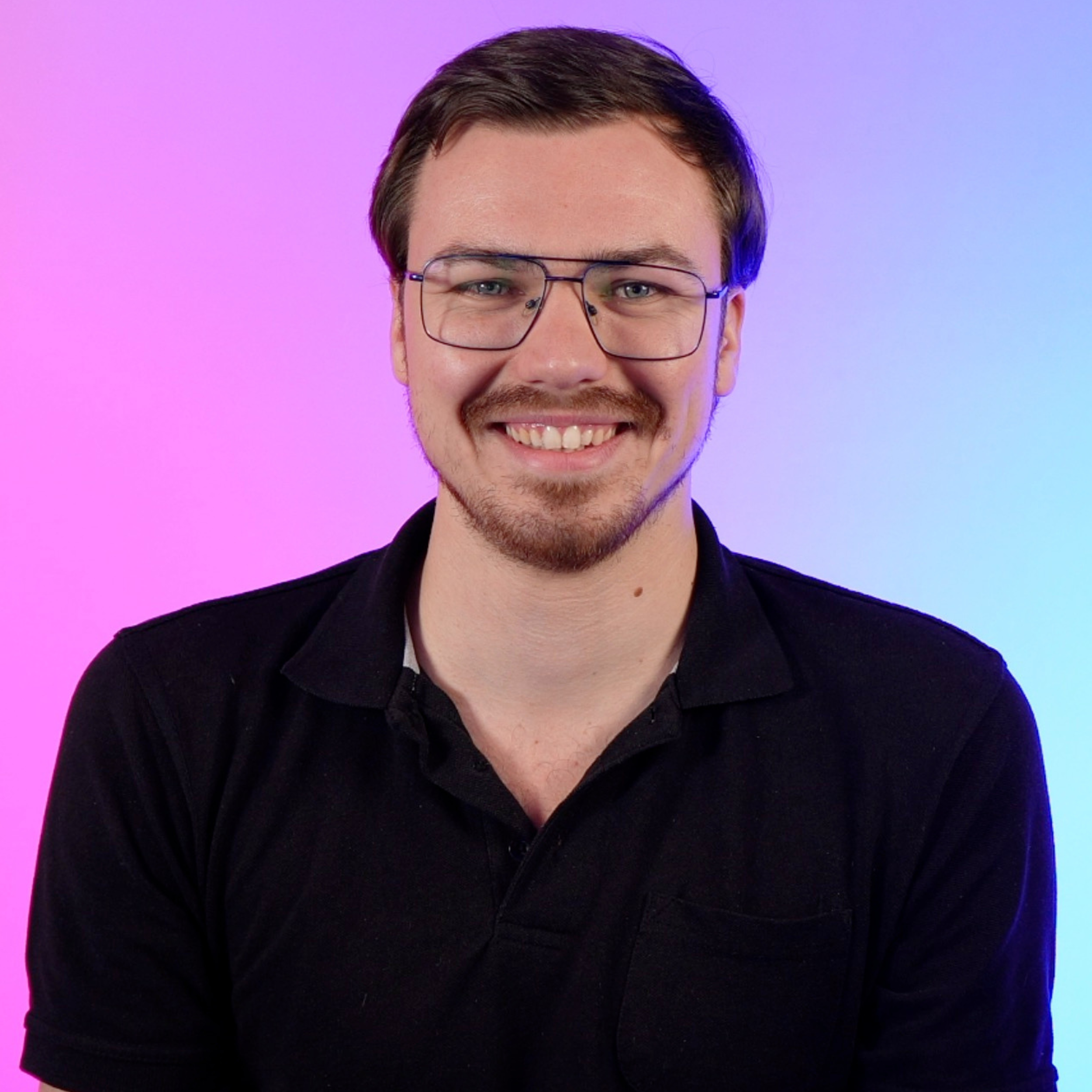 A young man with glasses, smiling, wearing a black polo shirt against a gradient pink and purple background.