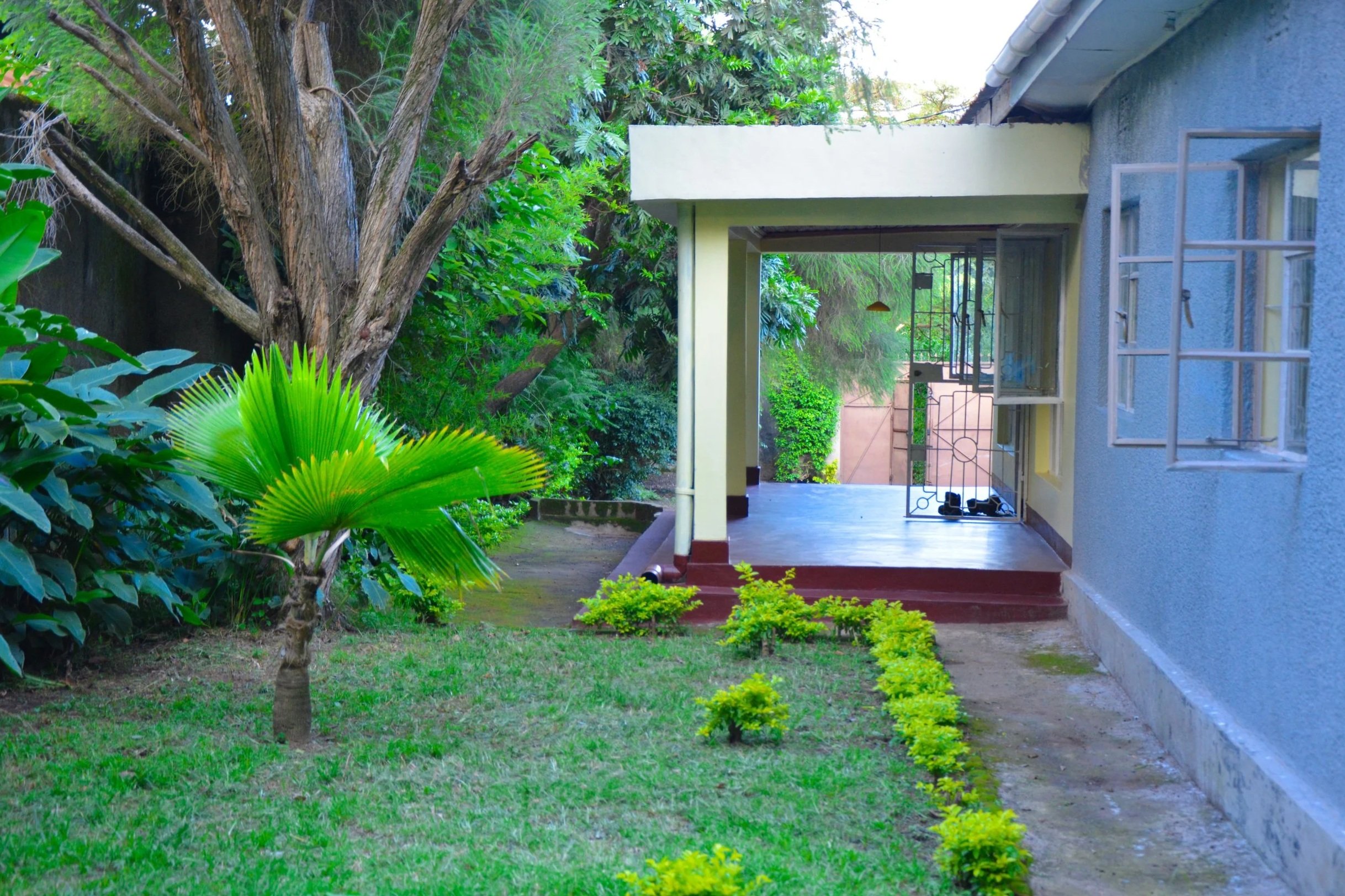A scenic landscape with a lake in the foreground, rolling hills covered in grass and scattered bushes, and mountain peaks under a cloudy sky in the background.
