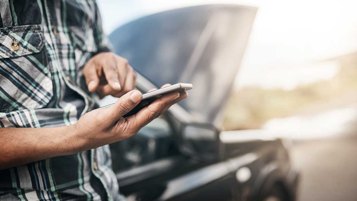Person in a plaid shirt using a smartphone near a car.