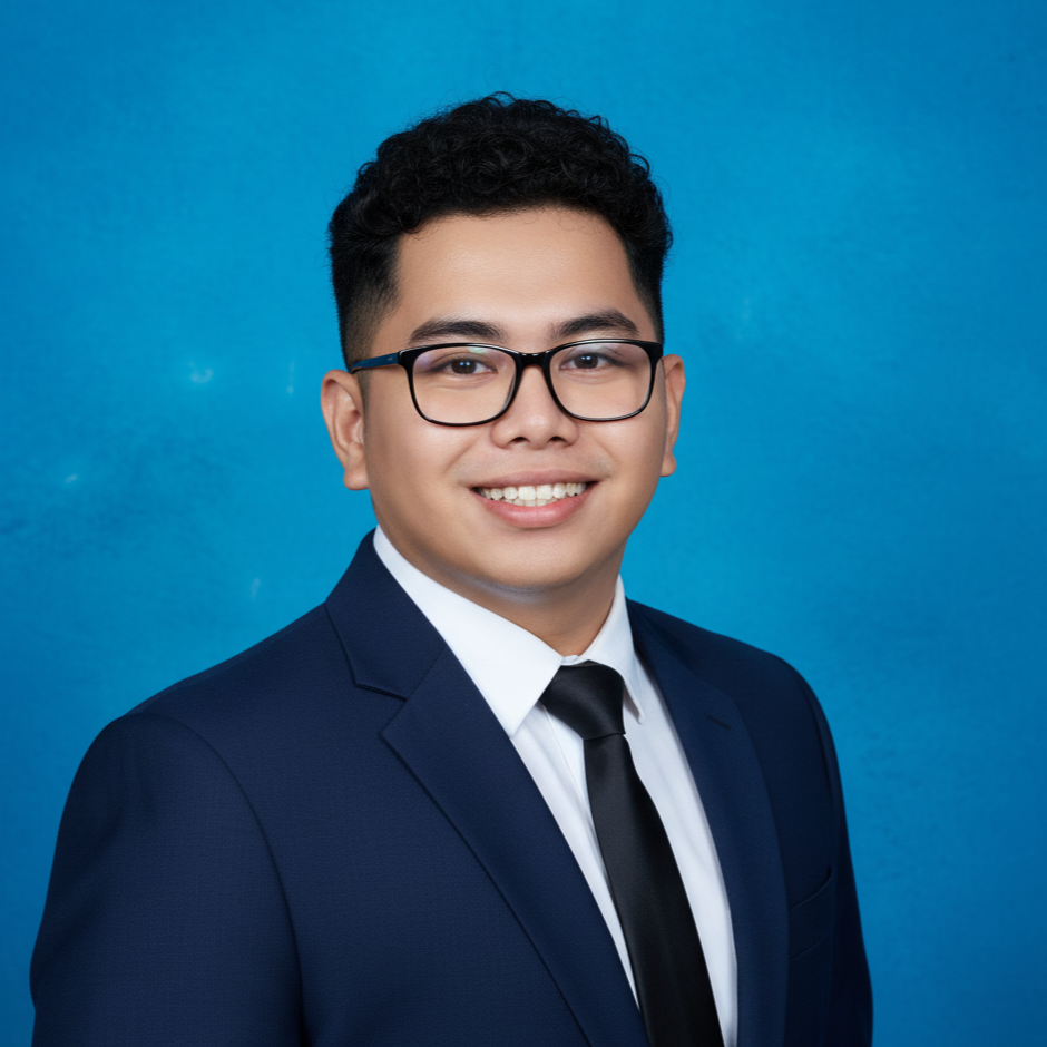 Professional headshot of a young man in a suit and tie, wearing glasses, smiling against a blue background.