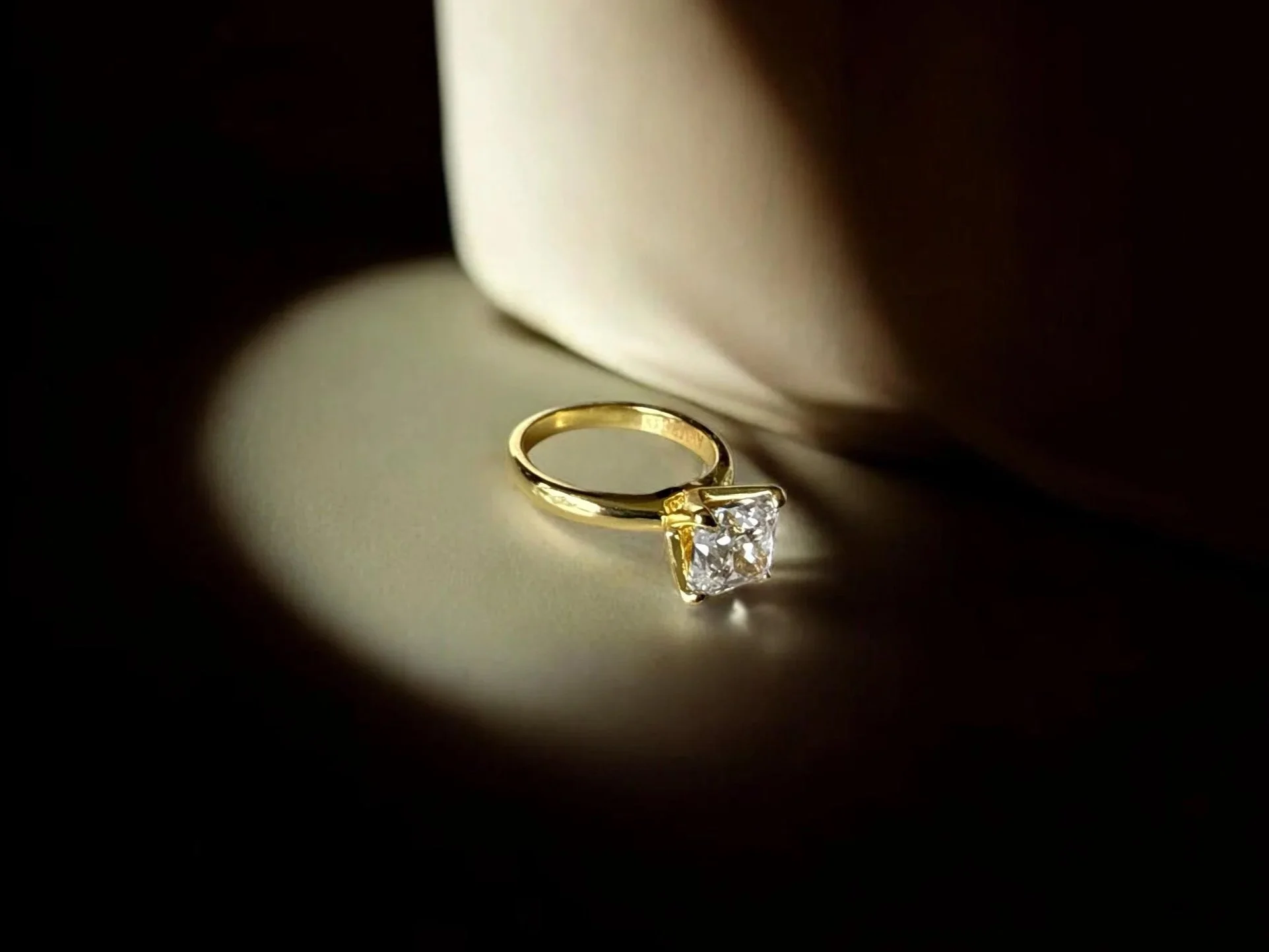 A gold ring with a large square-cut diamond in a jewelry display with a dark background and a light-colored cloth or paper.