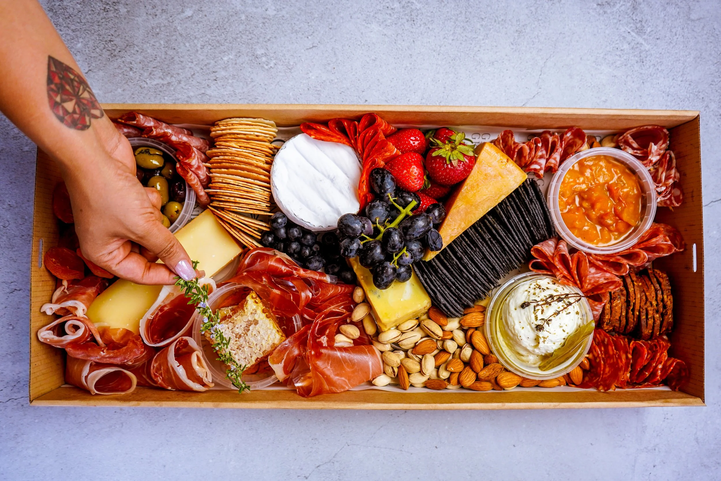 Charcuterie board with cheese, crackers, grapes, strawberries, strawberries, olives, and assorted meats in a wooden box.