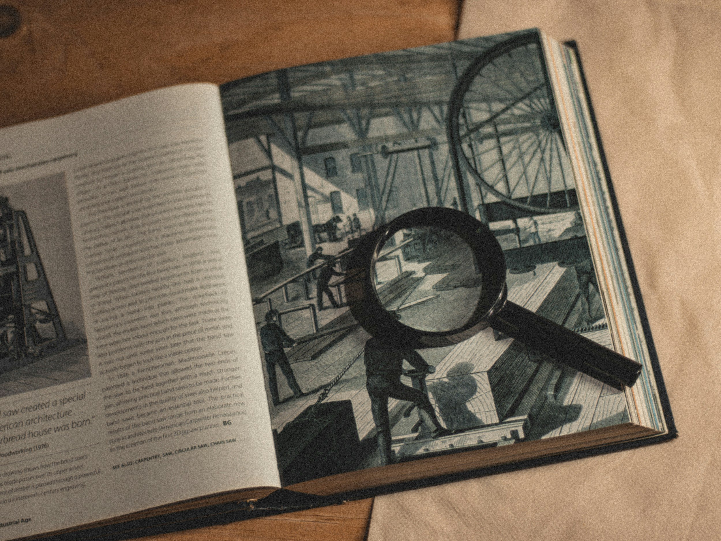 Open book showing black and white illustration of a construction site with workers and a large circular saw, magnifying glass placed over the illustration.
