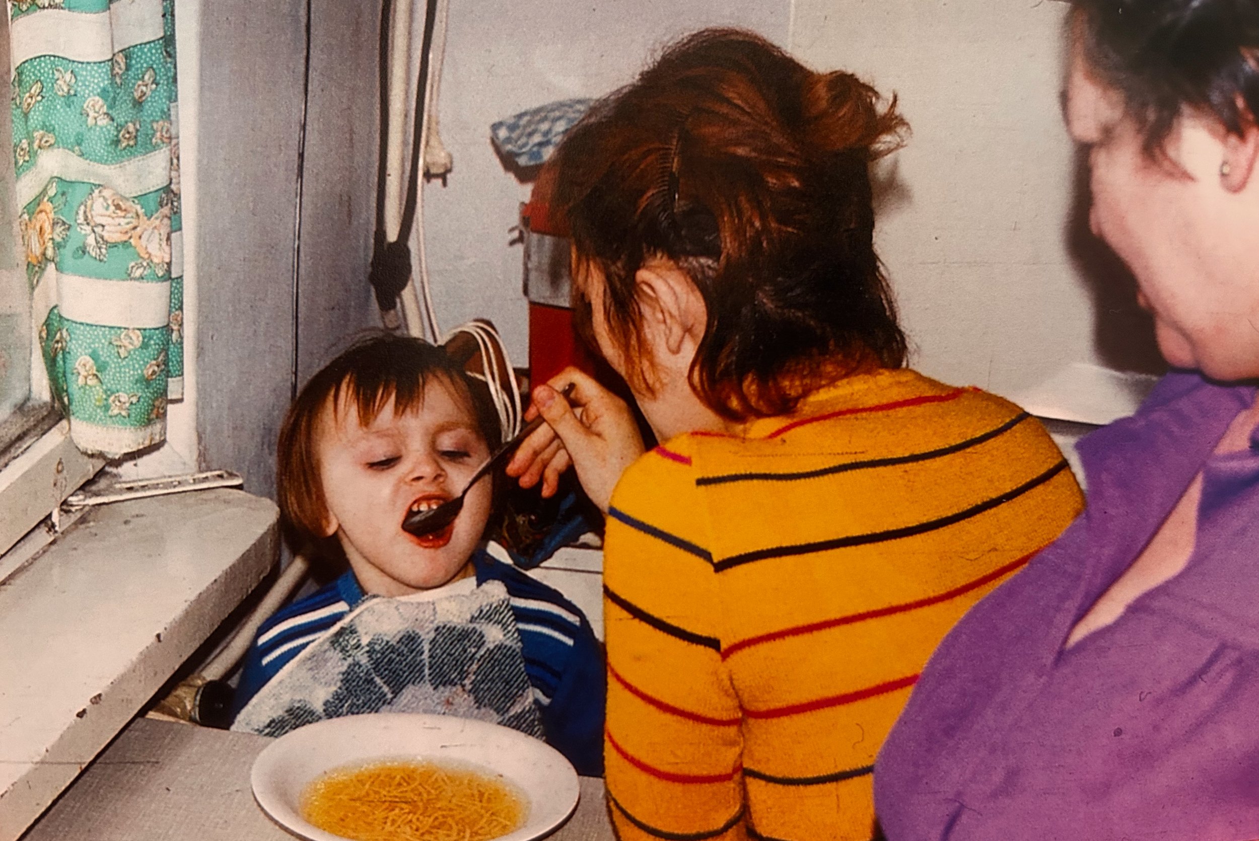 Kind wird von Mutter und Großmutter am Küchentisch beim Essen gefüttert, 1970er/80er Jahre, familiäre Alltagsszene in Polen.