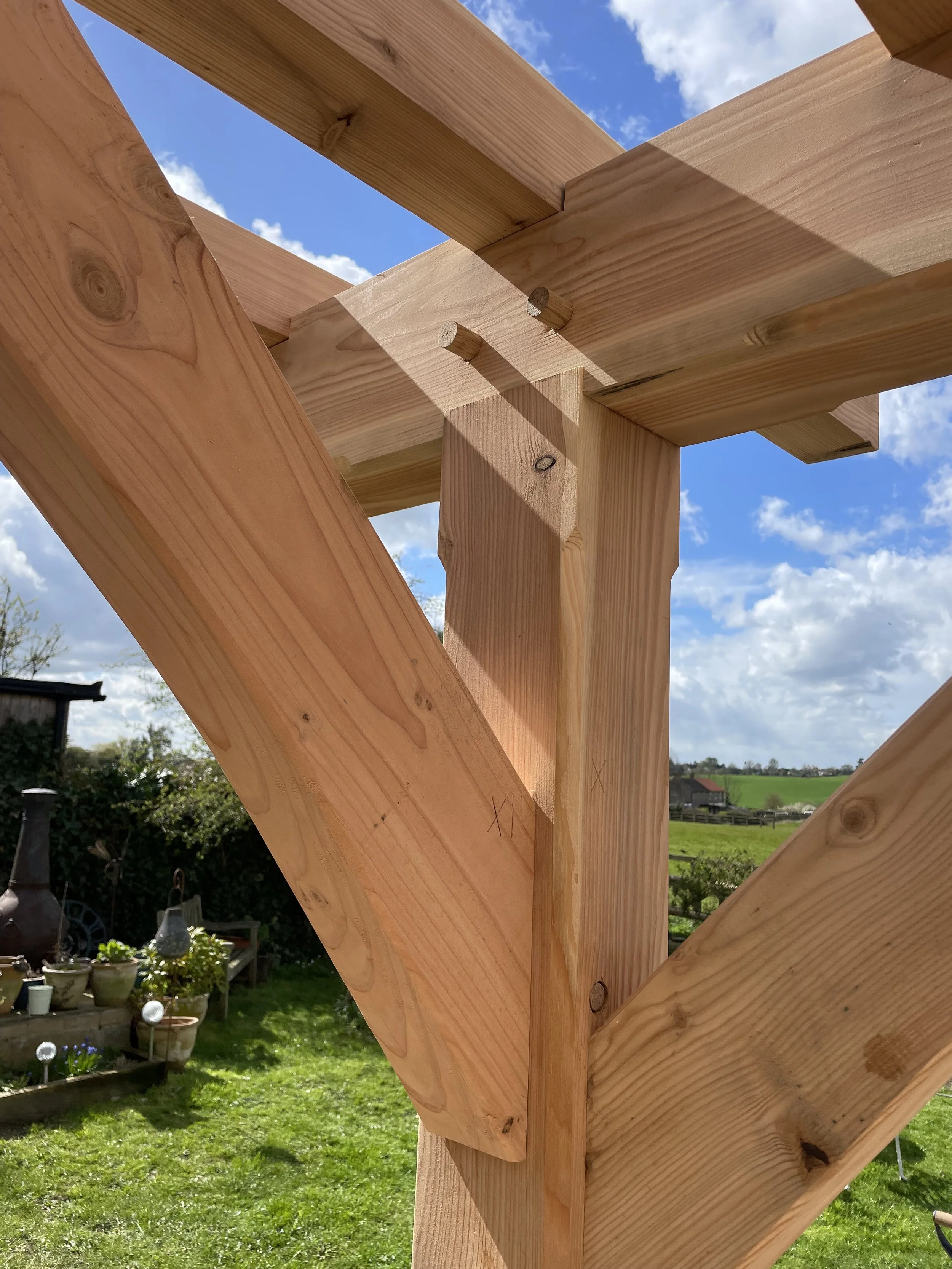 Close-up of wooden construction framing with a background of a grassy yard and blue sky with clouds.