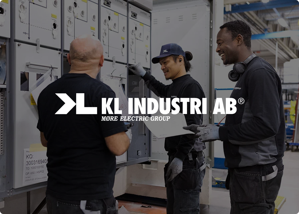 Tre arbeidere i arbeidsuniform foran elektrisk kontrollpanel i industrianlegg.