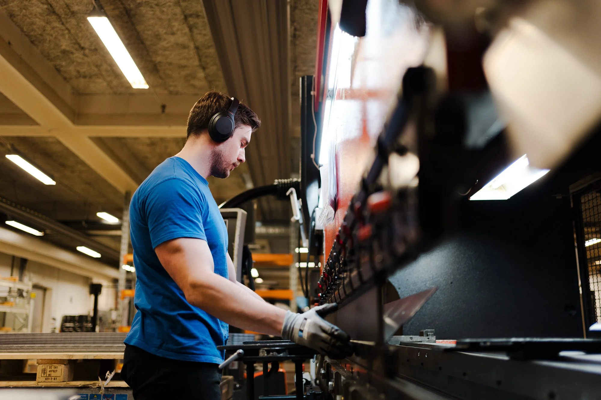 Ung arbeider med hansker og hørselvern ved stor industrimaskin i verksted.