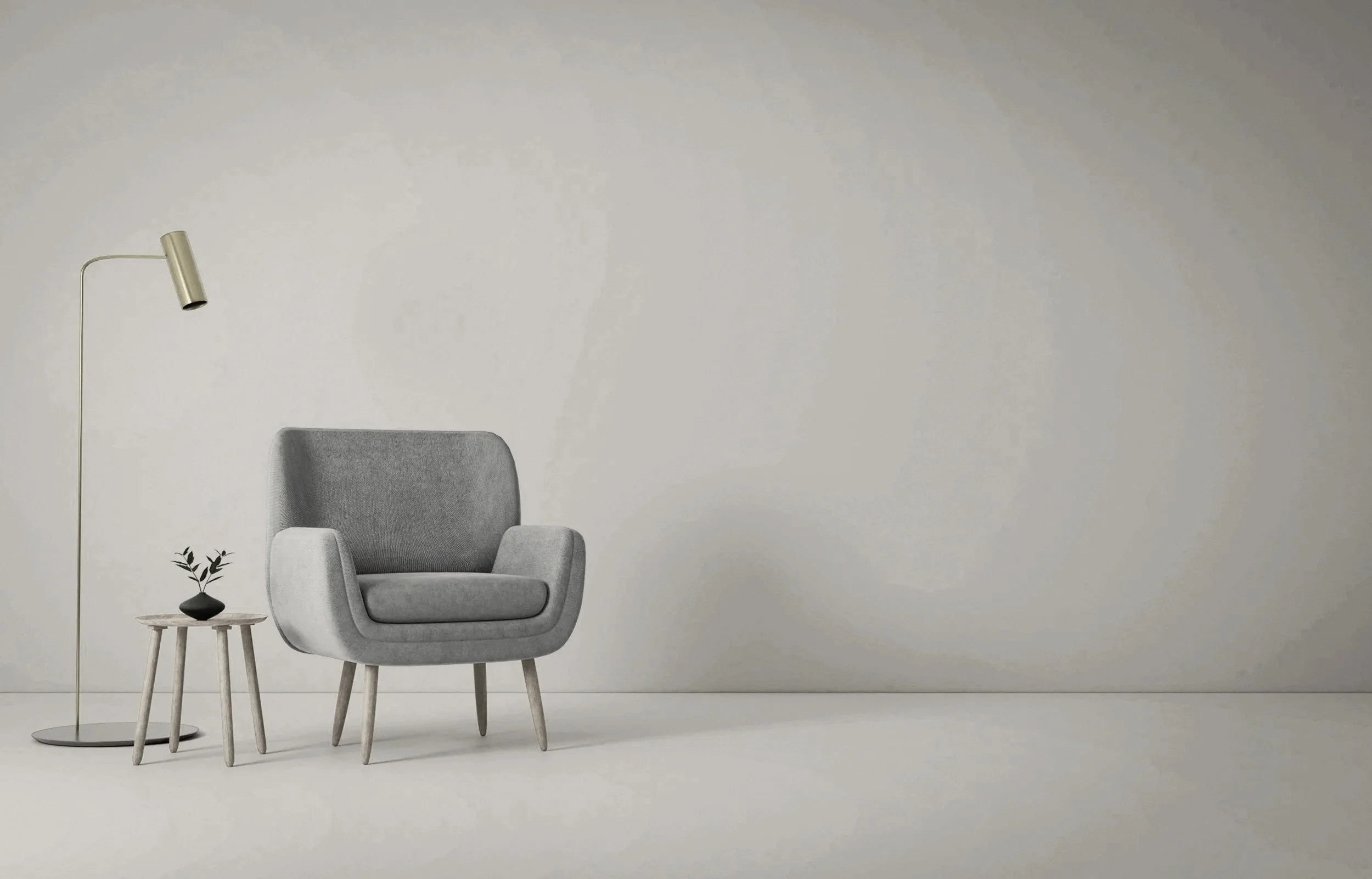 A minimalist living room corner with a gray armchair, a small wooden side table with a black vase and plant, and a tall, curved floor lamp against a plain off-white wall.
