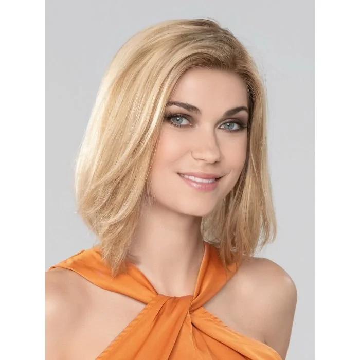 Close-up of a young woman with blonde hair, blue eyes, and a slight smile, wearing an orange top with a knot at the neck, against a plain gray background.